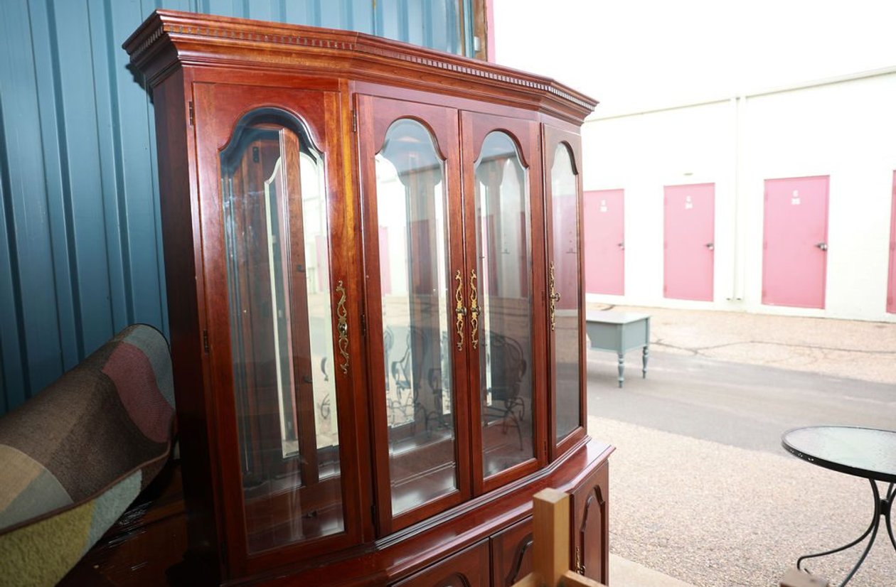 Large cherry wood china cabinet with 4 arched glass doors, interior lighting, brass hardware, and dentil crown molding